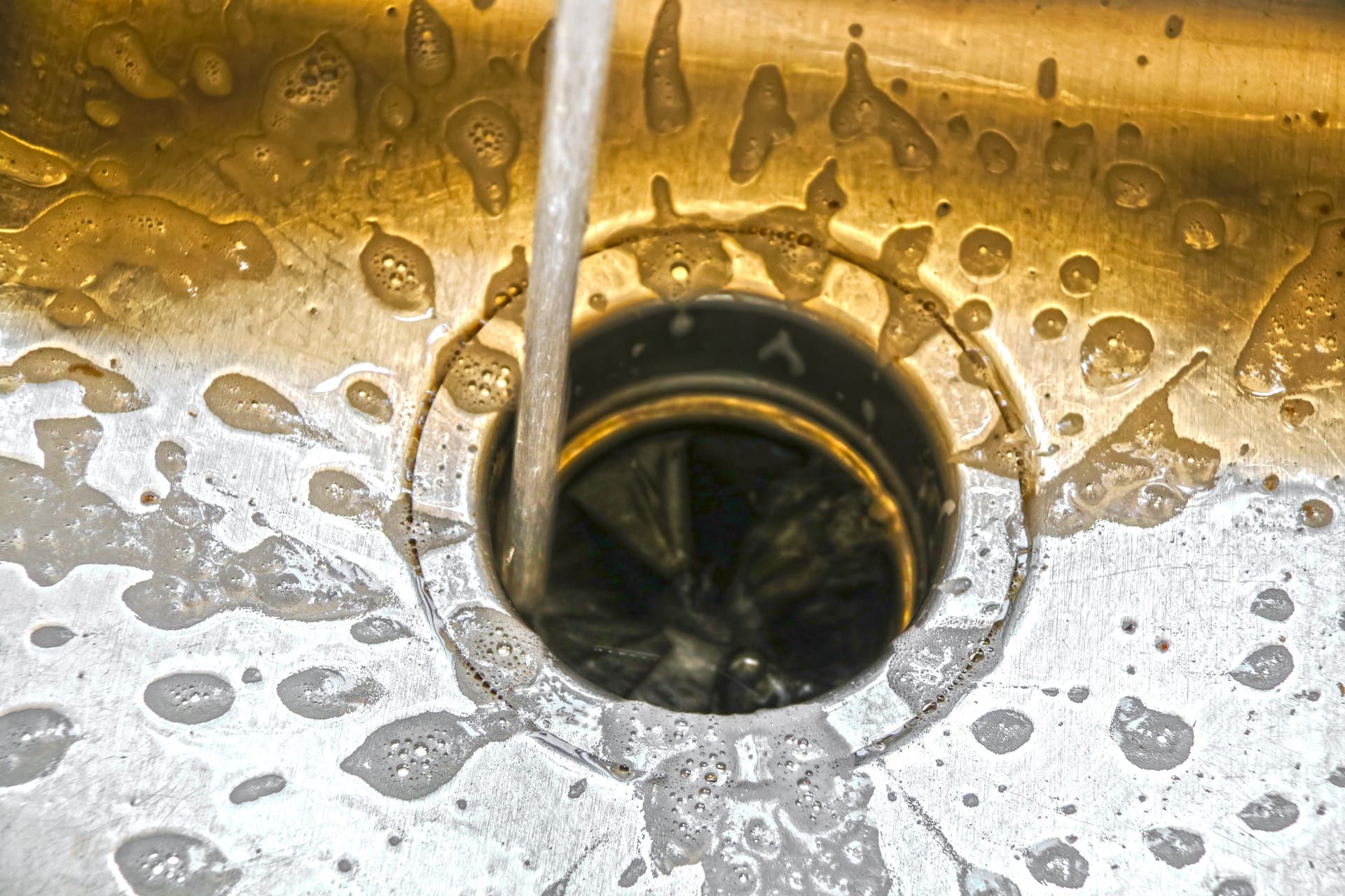 Water running into a garbage disposal drain in a stainless steel sink